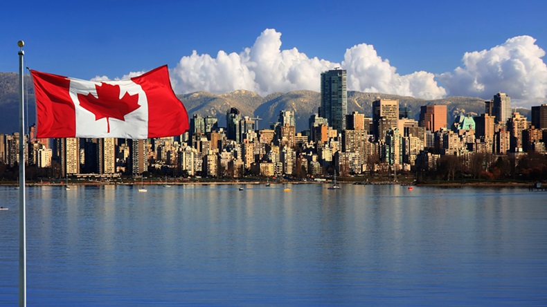 Flag of Canada flies over water with cityscape in background