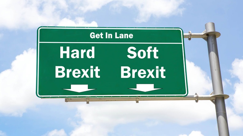 Green overhead road sign with the instruction to get in lane with a Hard Brexit or Soft Brexit concept against a partly cloudy sky background.