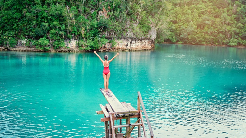 Vacation and activity. Young woman in swimsuit enjoying blue tropical lagoon view standing on wooden springboard. Siargao Island, Philippines.