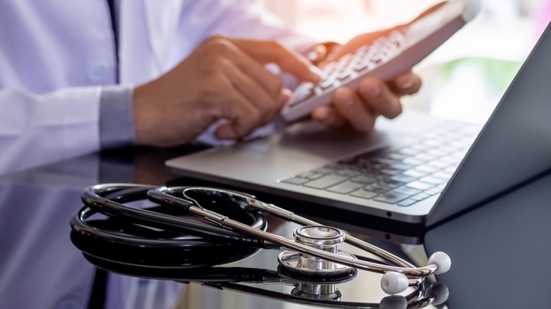 Male doctor or practitioner using calculator and work on laptop computer with medical stethoscope on the desk at clinic or hospital. Medical healthcare costs ,fees and revenue concept. - Image 
