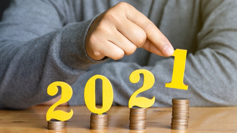 2021 New year saving money and financial planning concept. Female hands putting gold wooden number 2021 on stack of coins. tax payment, investment and banking.