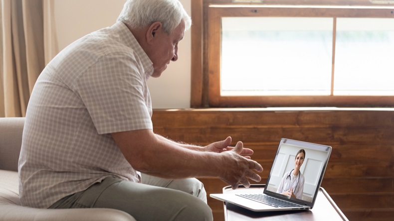 Elderly 70s man seated on sofa make distant video call, senior patient look at laptop screen communicating with doctor therapist online, older generation and modern tech application easy usage concept