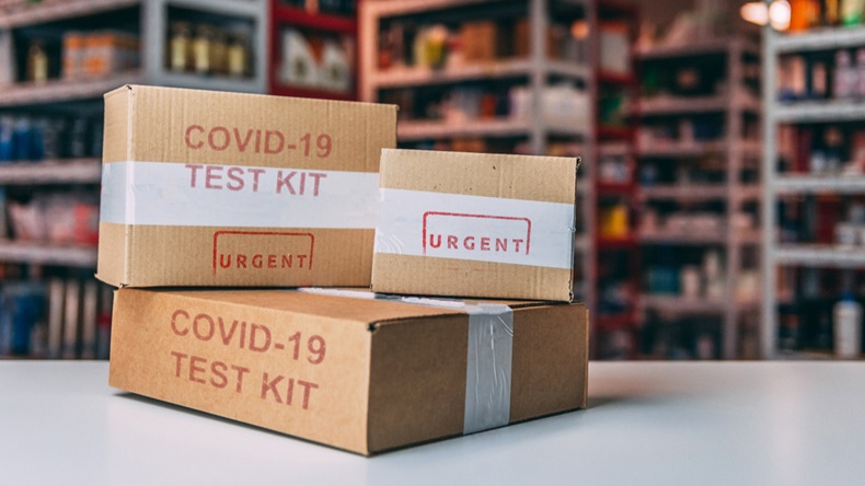 Concept of the impact and threat of the corona virus health crisis, boxes of coronavirus tests kit in front of purposely blurred drugstore shelves in the background.