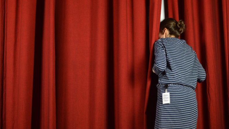 woman with a backstage pass looking behind the red curtains on a stage