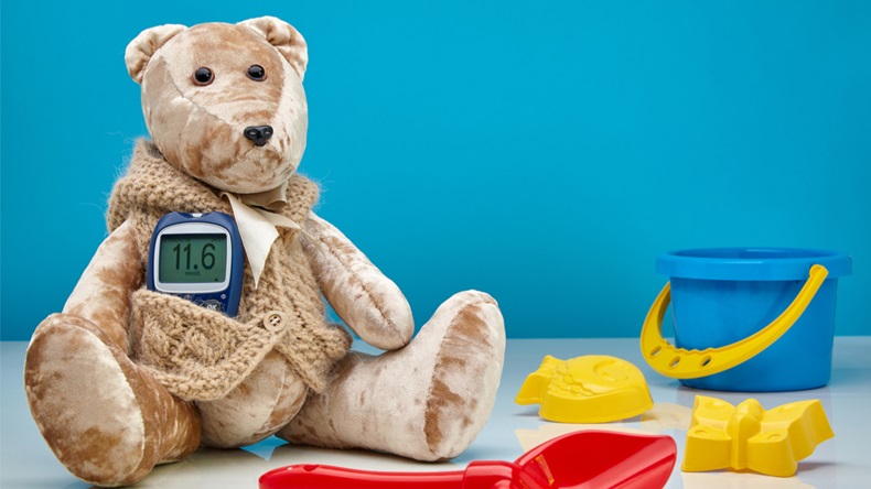 Teddy bear with a glucometer and scattered children's toys on a blue background. The concept of treatment of diabetes in children, hyperglycemia, pediatric doctor