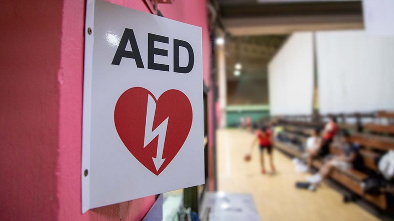 An automated external defibrillator symbol in front of the gymnasium. The AED using in emergency situation such as acute cardiac arrest. The basketball players was playing in blurred background.