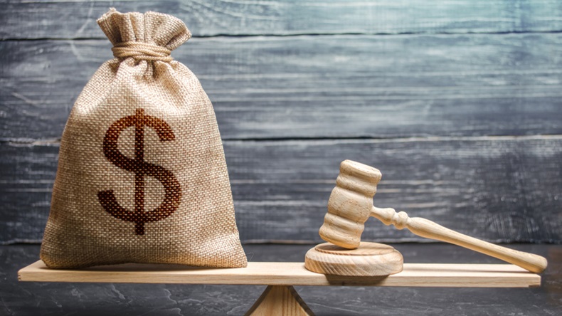 A bag of money is balanced on a scale against a wooden gavel.