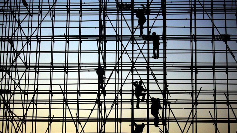 Construction workers climb scaffolding against an evening silhouette.