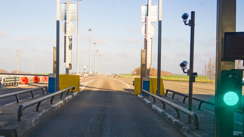 Open barrier at a checkpoint on a toll road. Green traffic light allowing traffic. View through a car windshield.