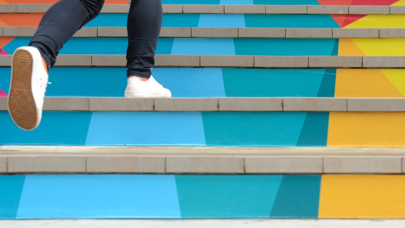 Lower part of teenage girl in casual shoe walking up outdoor colorful stairs.