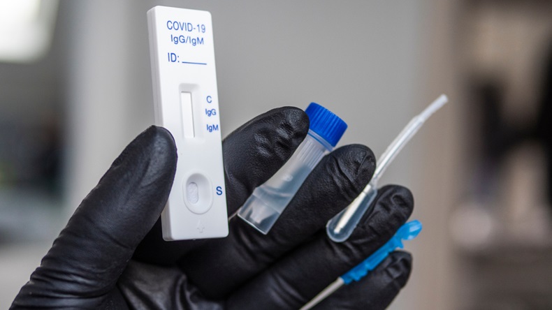 Covid-19 test kit for detecting IgM/IgG antibodies and immunity in 15 minutes, held in hand wearing a disposable glove.