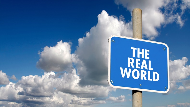 A sign with the words "The Real World" with a cloudy sky backdrop