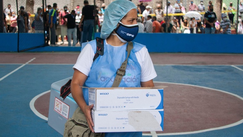 A nurse in blue protective gear carries boxes of COVID-19 vaccine in Caracas, Venezuela.