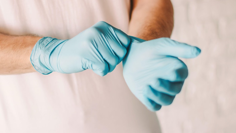 Closeup of professional doctor putting on blue latex gloves on hands. 