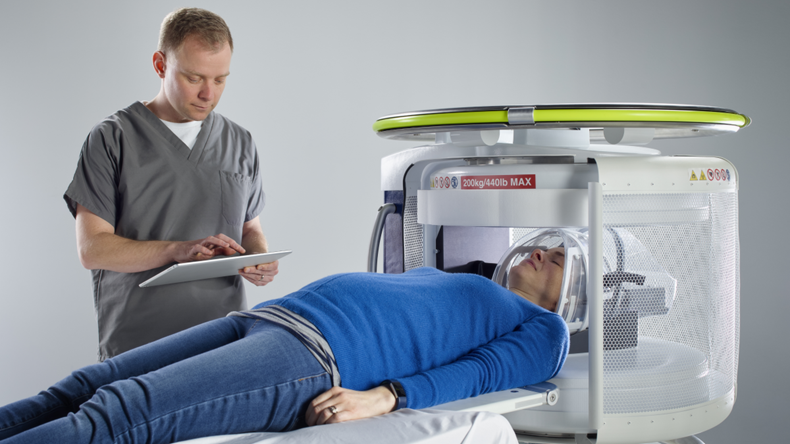 Patient's head being scanned by Hyperfine's portable magnetic resonance imaging system, controlled by tech using an iPad