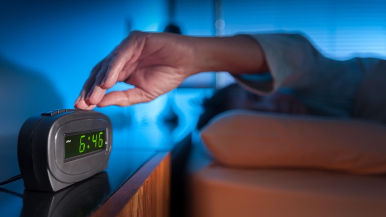 Woman pressing snooze button on early morning digital alarm clock