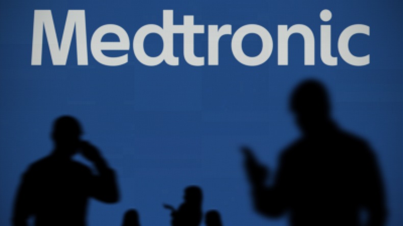 The Medtronic logo is seen on an LED screen in the background while a silhouetted person uses a smartphone in the foreground.