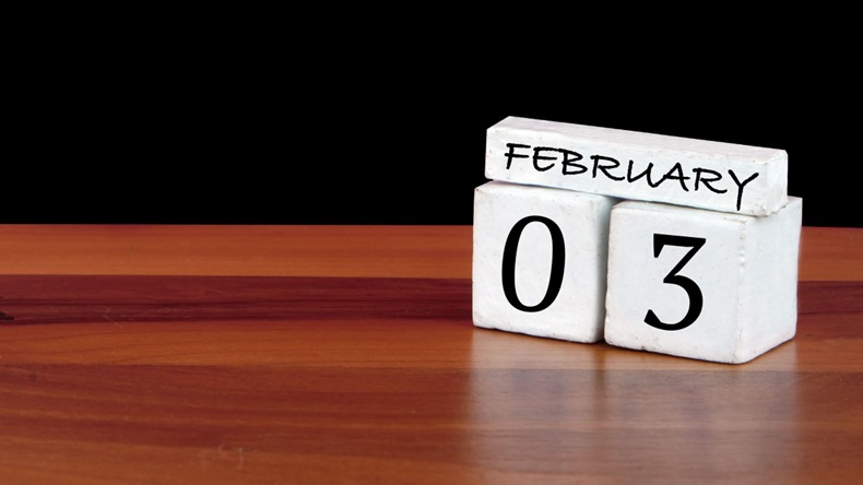 A block calendar reading 3 February on wooden table with black background