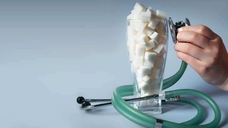 A hand holds a stethoscope up to a tall vase full of white sugarcubes.