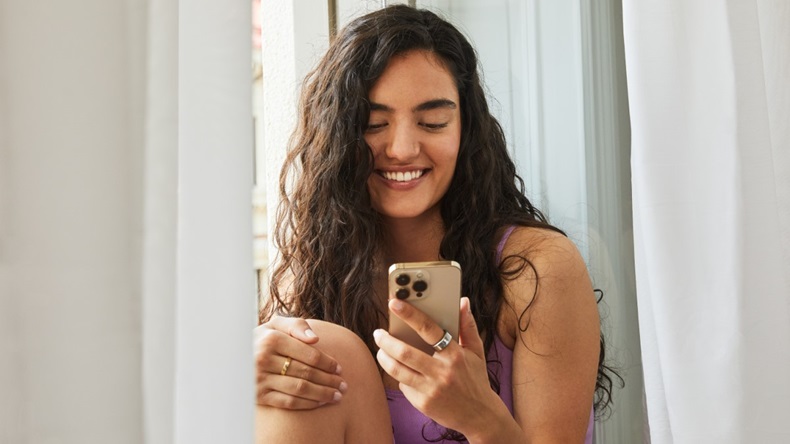 Smiling young woman holding smartphone and wearing Oura Ring.
