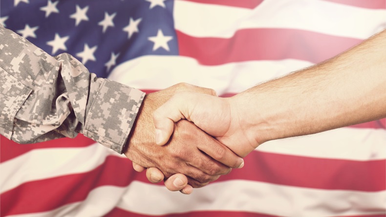 A handshake between a person in a military uniform and a civilian in front of the US flag.