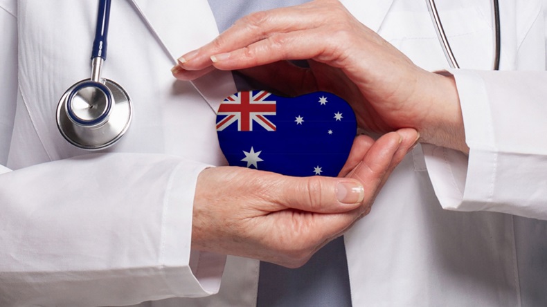 Chest of doctor wearing a white coat with hands around a heart-shaped Australian flag.