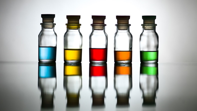 Five bottles with diverse colors of content reflected on a table